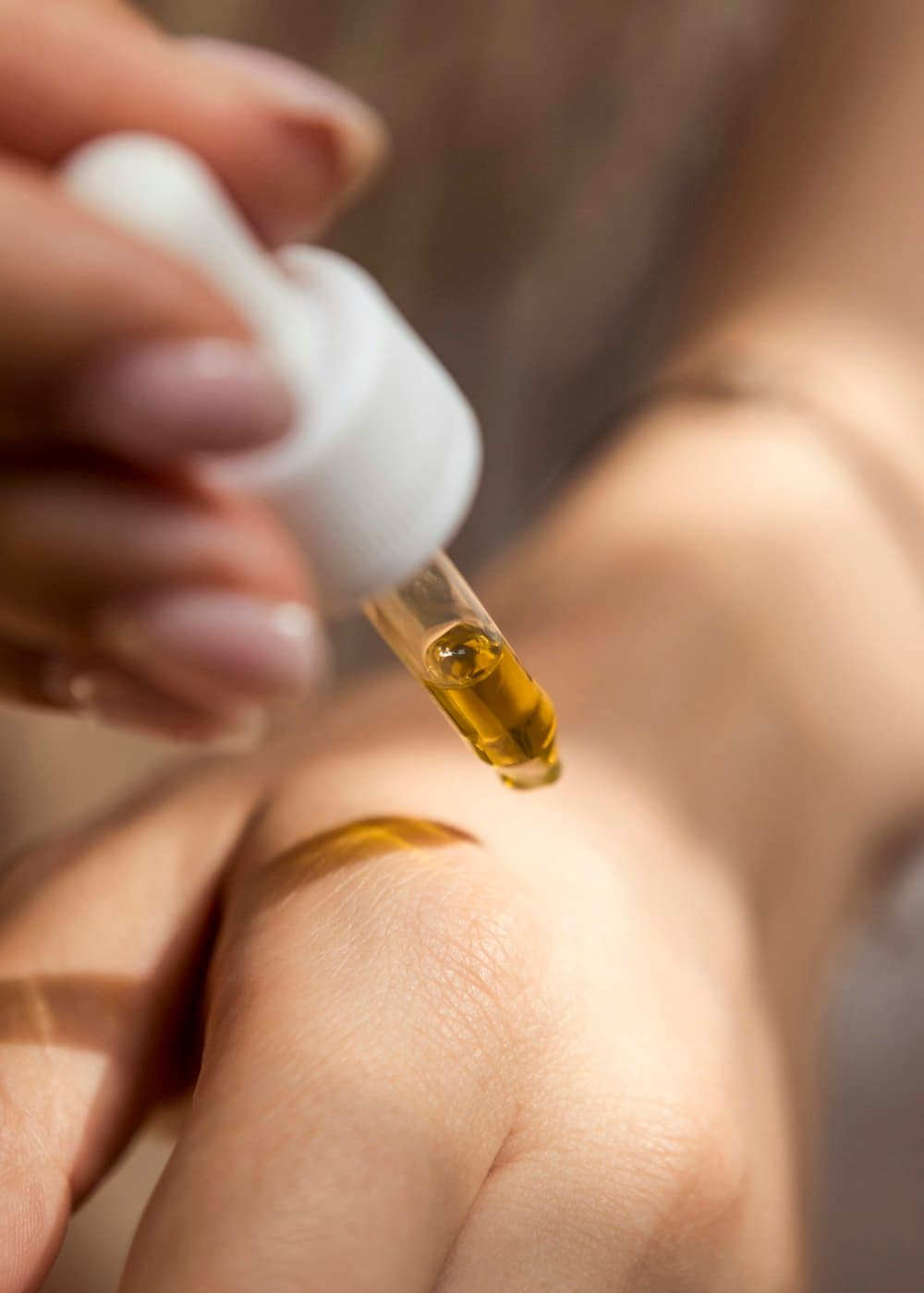 Gota de sérum dourado caindo do conta-gotas sobre a pele
